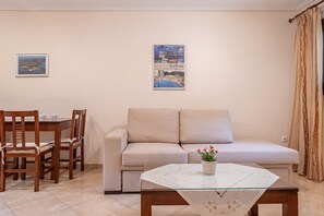 Un salon comprenant un canapé, une table basse en verre, une table à manger avec des chaises et deux tableaux encadrés accrochés au mur.