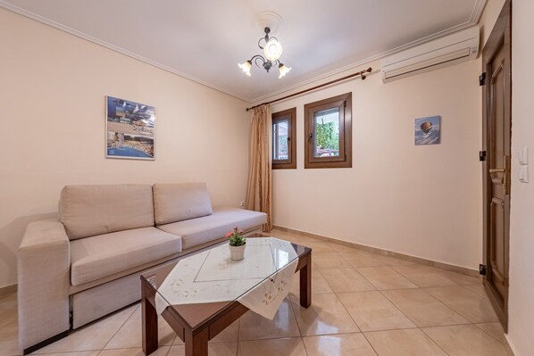 A living room with a sofa, a glass-top coffee table, two windows, and a ceiling light fixture.