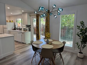 Et moderne køkken med hvide skabe, et spiseområde med et rundt bord og en loftlampe.