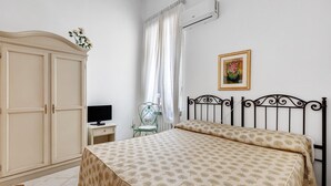 A bedroom with a bed, a wardrobe, a desk, a chair, and a picture on the wall.