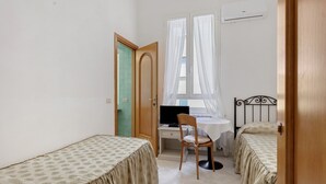 A small room with two beds, a desk with a computer, a chair, and a window with curtains. - Room 'Camera 45' with Wi-Fi and Air Conditioning (Verona)
