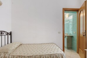 Een slaapkamer met een bed, een houten deur en een zichtbare badkamer door een geopende deur.