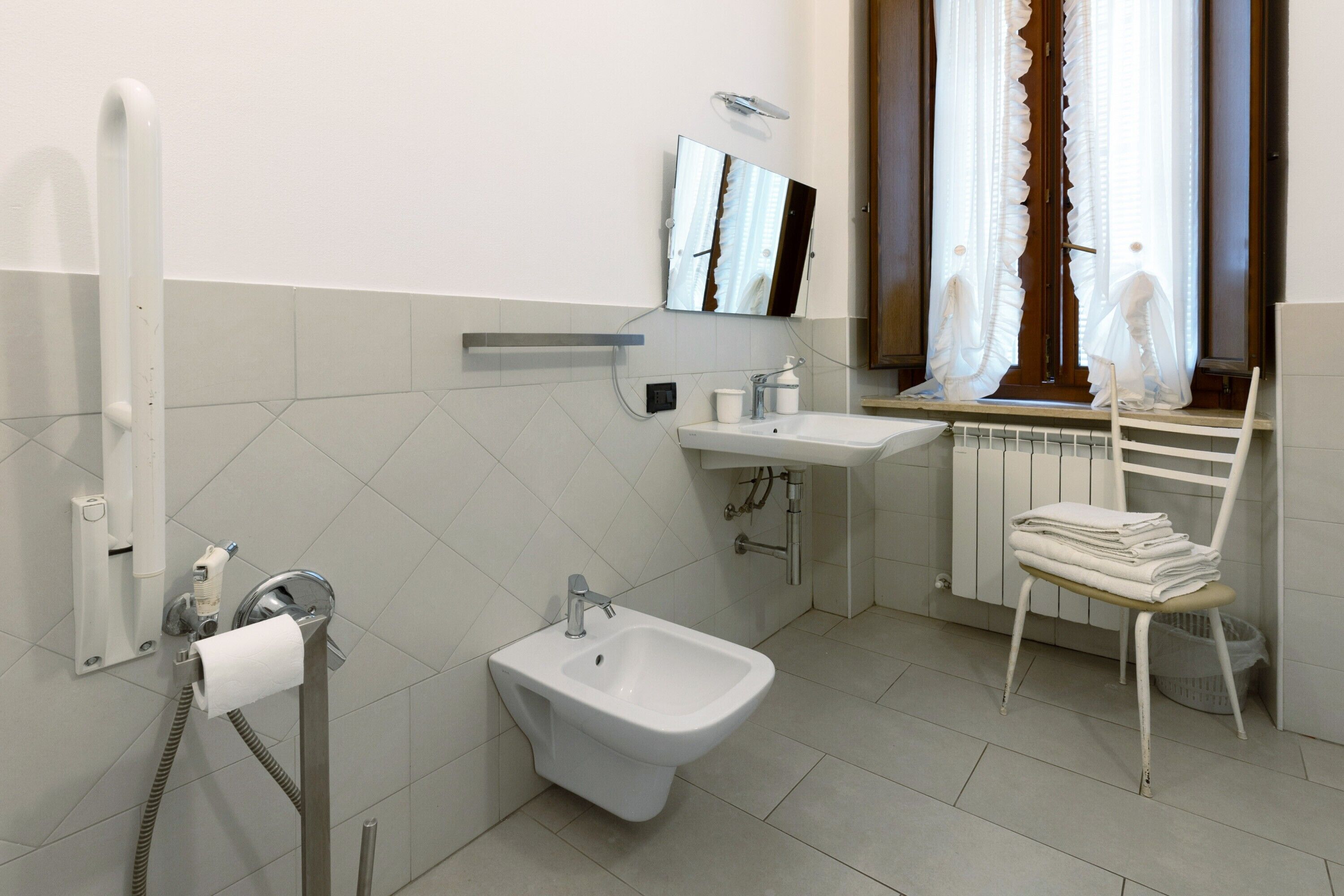 Un bagno con bidet, lavandino, specchio e finestra con tende.