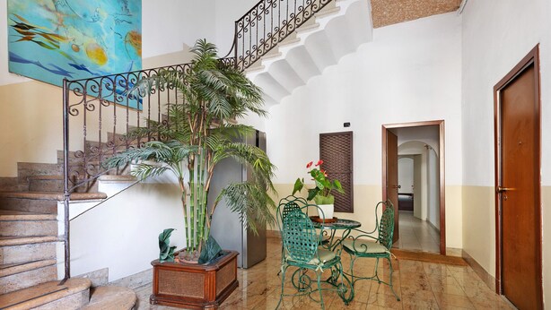 A staircase with a metal railing, a potted plant, a green chair, a small table with a vase, and a door. - Room 'Camera 48' with Wi-Fi and Air Conditioning (Verona)