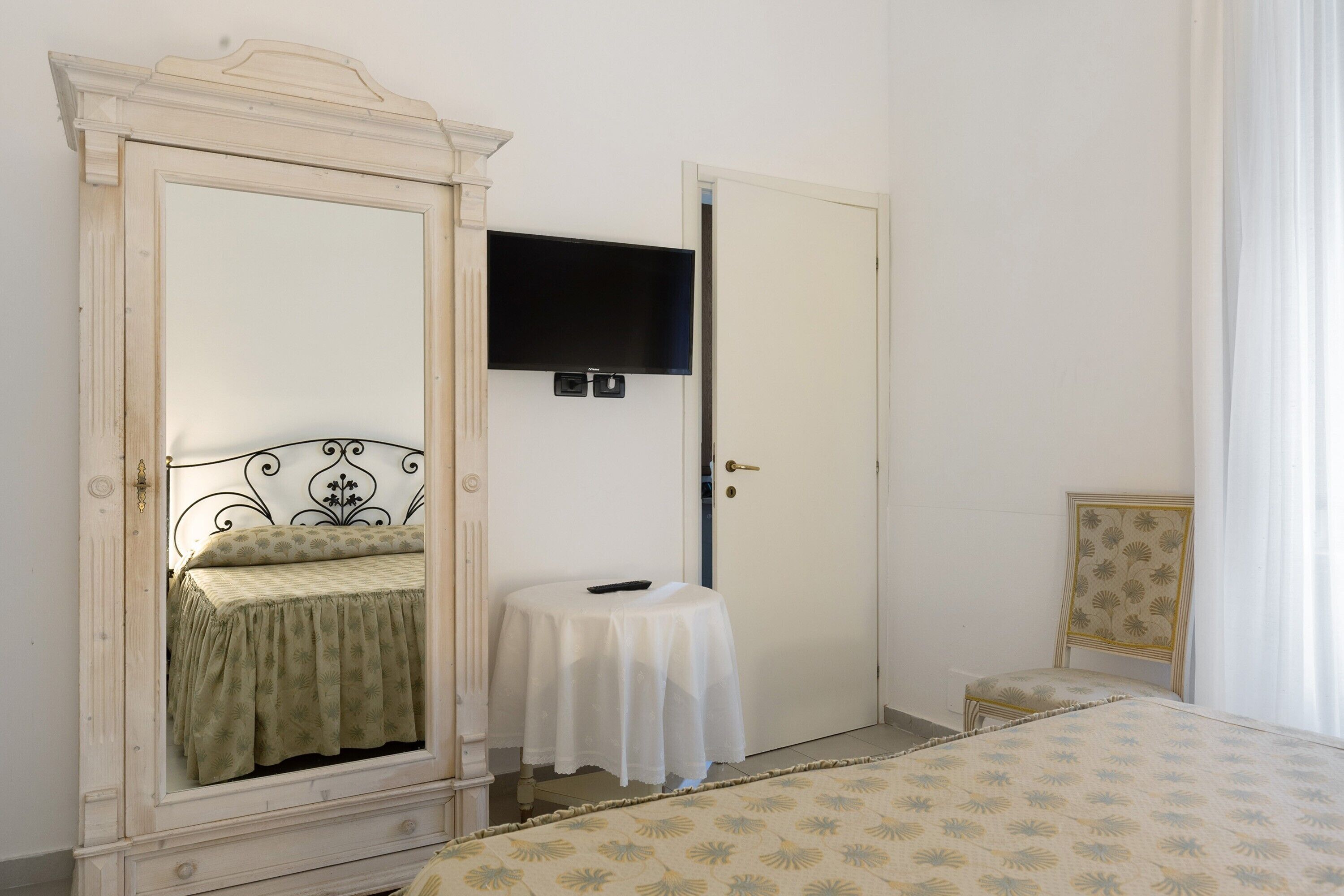 Una camera da letto con un letto, un comodino, uno specchio, una televisione e una porta.