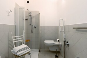 Een kleine badkamer met een douche, toilet en een stoel met handdoeken.