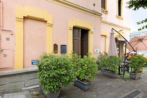 A building with a yellow facade, a closed door, and potted plants in front.