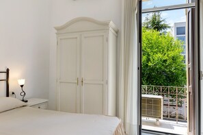 A bedroom with a bed, nightstand, and wardrobe, with a view of a balcony and trees.
