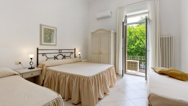 Une chambre avec deux lits, une table de chevet, une commode et une fenêtre donnant sur un paysage verdoyant.