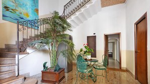 Un escalier avec une rampe en métal, une plante en pot, une chaise verte, une petite table avec un vase et une porte.