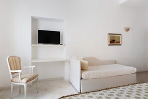 Een kamer met een bed, een stoel, een televisie op een plank en een ingelijst beeld aan de muur.