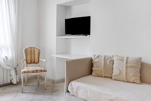 Een kamer met een bed, een stoel, een televisie op een plank en een raam met gordijnen.