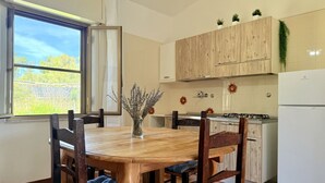 A kitchen with wooden cabinets, a dining table with chairs, a refrigerator, and a window with a view of trees.