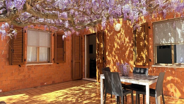 An outdoor patio with a brick wall, wooden shutters, and a table with chairs.