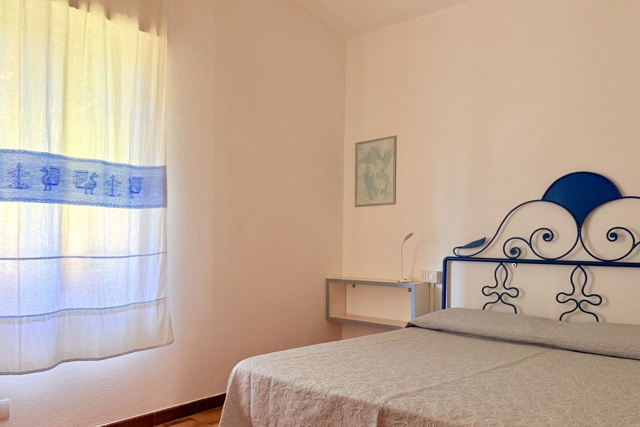 Una camera da letto con un letto, un comodino, una mensola a muro e una finestra con tende.
