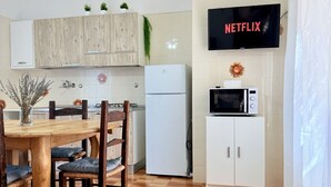 A modern kitchen with wooden cabinets, a white refrigerator, a microwave, and a TV displaying "NETFLIX".