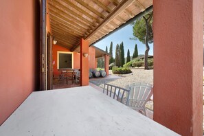 An outdoor patio with a white table and chairs, a wooden pergola, and a view of a garden with trees and a gravel path.