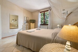 A bedroom with a bed, a bedside lamp, a mirror, a window with curtains, and a wall-mounted plant.