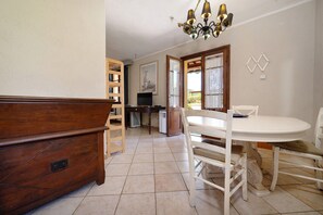 A dining area with a white table and chairs, a wooden cabinet, and a television in the background. - 'Merlot' Apartment with Shared Pool, Private Terrace, and Communal Garden (Suvereto)