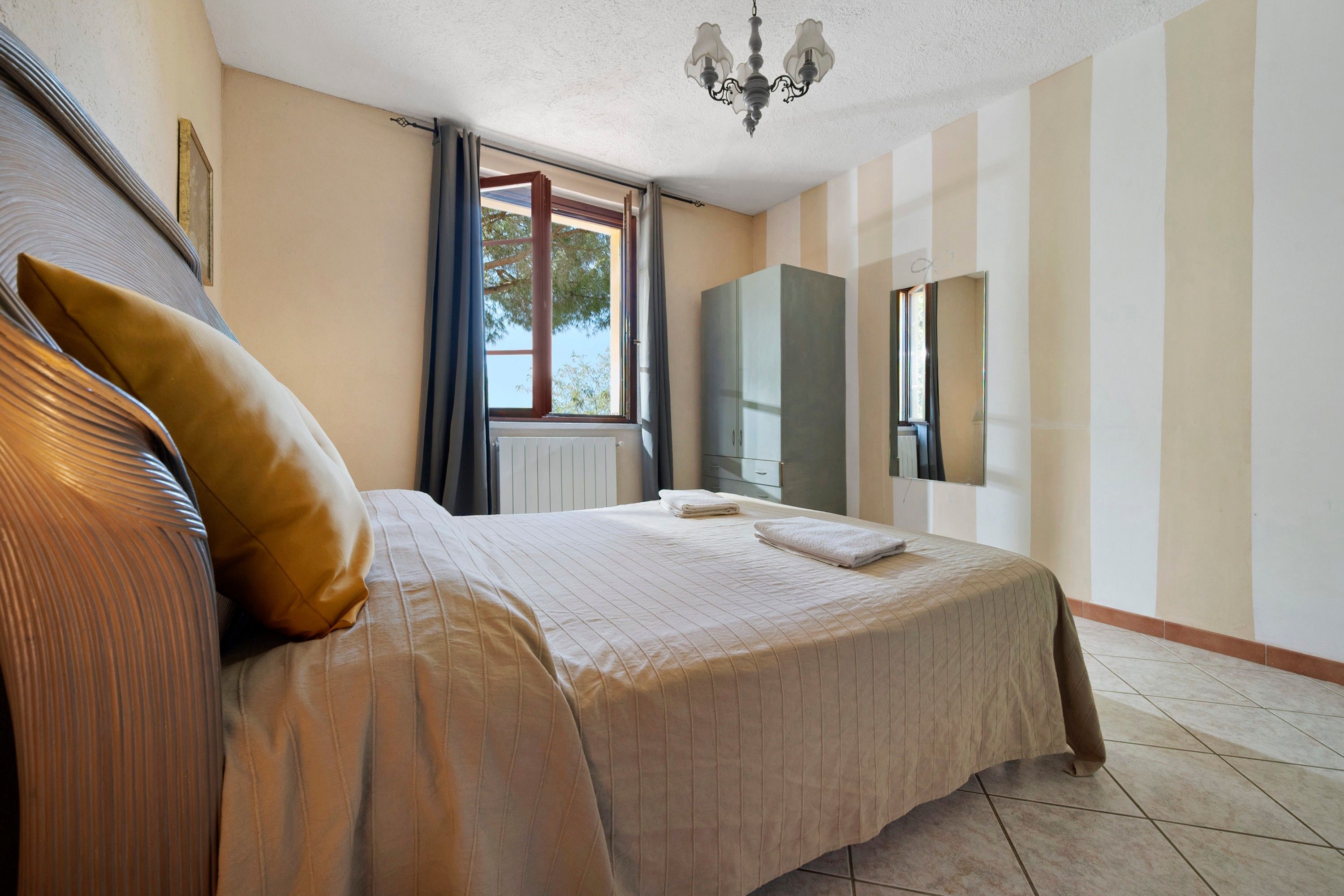 Una habitación de hotel con una cama grande, una ventana con cortinas, un radiador, un armario y una araña.
