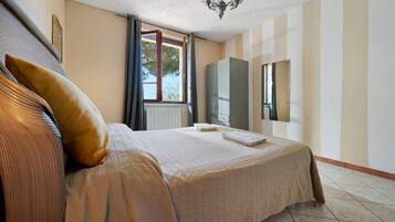 Una habitación de hotel con una cama grande, una ventana con cortinas, un radiador, un armario y una araña.