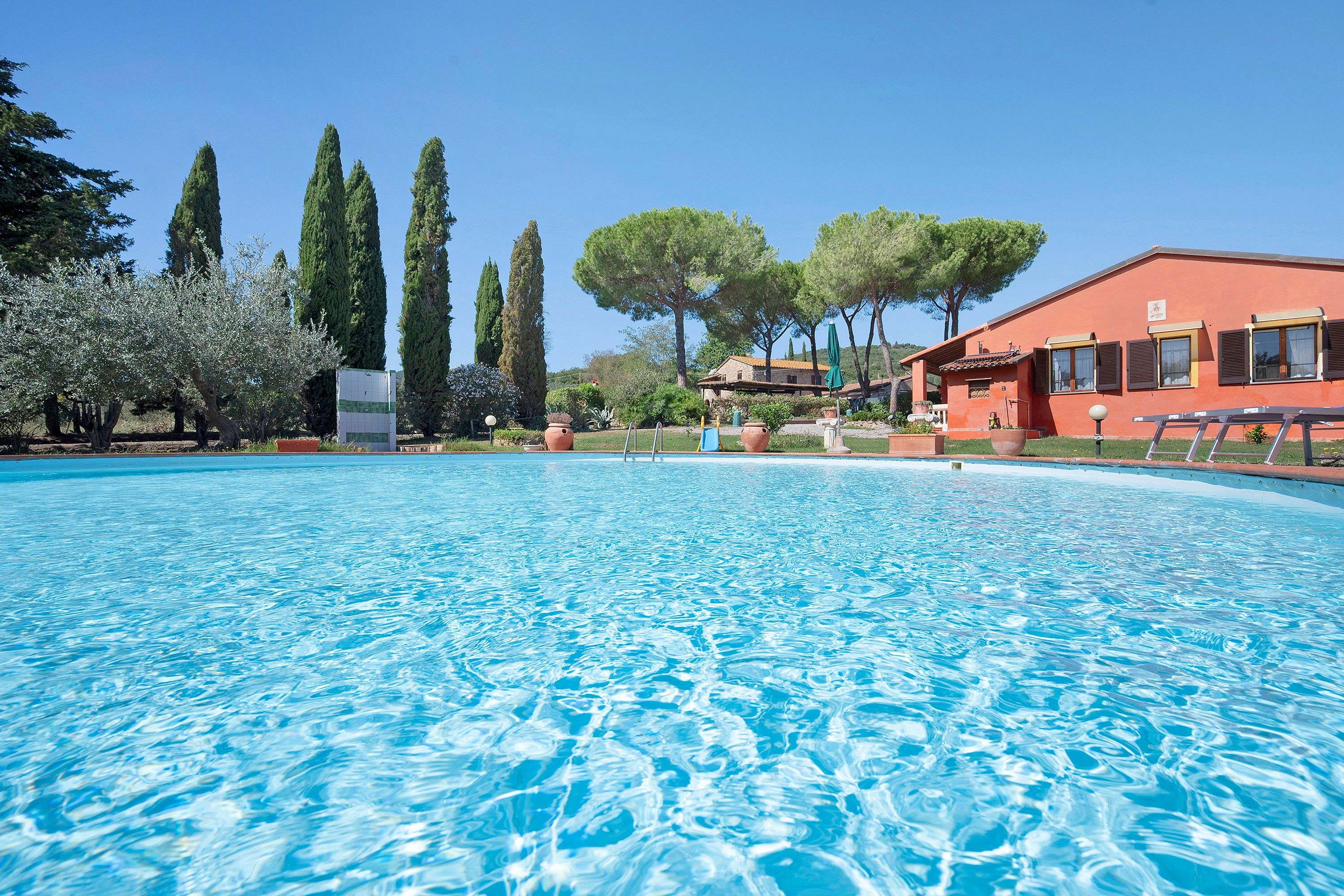 A swimming pool with clear blue water, surrounded by trees and a building with a red facade.