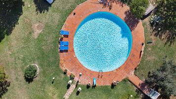 Una vista aerea di una piscina circolare con un bordo piastrellato, panchine e un piccolo giardino.