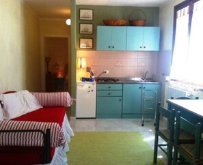 A compact kitchen with teal cabinets, a small dining area, and a bed with striped bedding.