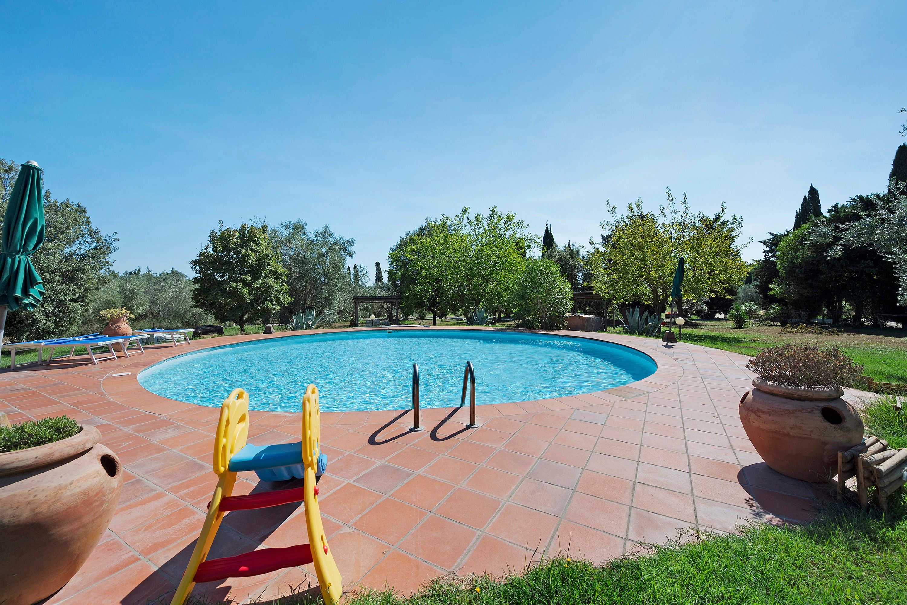A swimming pool with a tiled deck, a children's play structure, and potted plants.