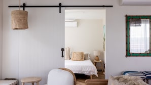 A room with a bed, a chair, a small table, and a hanging light fixture. - Sunbird Suite by Stay Noosa (Noosa Heads)