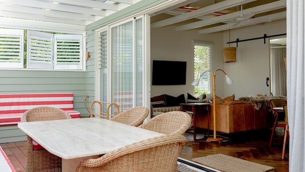 A room with a dining table, wicker chairs, a sofa, and a television. - Sunbird Suite by Stay Noosa (Noosa Heads)