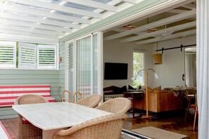 A room with a dining table, wicker chairs, a sofa, and a television. - Sunbird Suite by Stay Noosa (Noosa Heads)