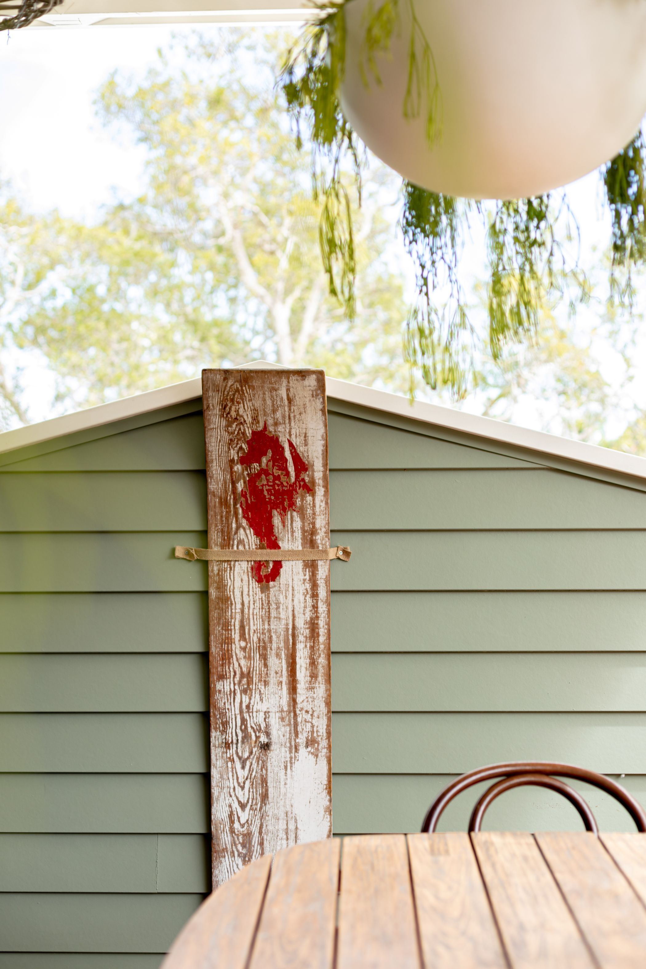 Une enseigne en bois ornée d’un cœur rouge, fixée à une maison dont le revêtement extérieur est vert.