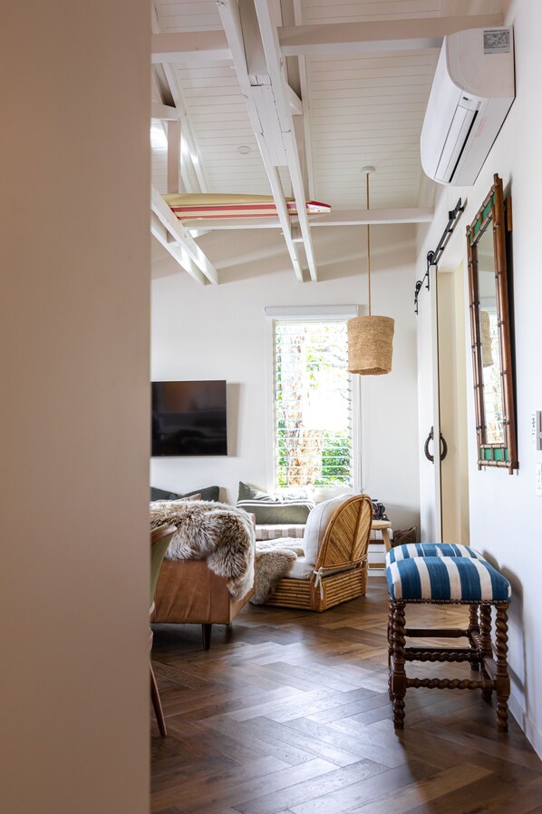 Una habitación con piso de madera, un sofá, una silla, una lámpara colgante y un aire acondicionado instalado en la pared.