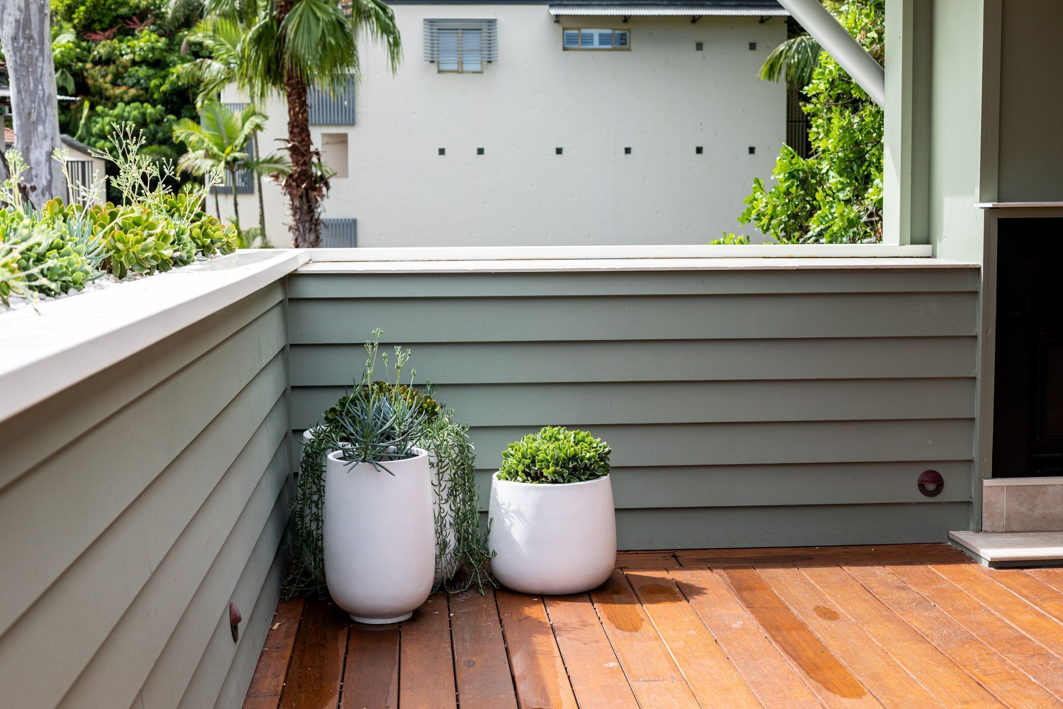 Une terrasse en bois avec deux jardinières blanches contenant des plantes.