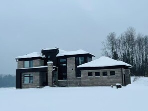 A modern two-story house with a stone facade, large windows, and a snow-covered roof.