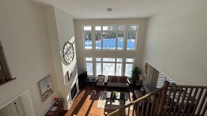 A spacious living area with a fireplace, large windows, and a staircase.