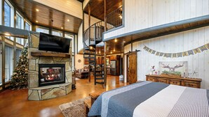 Un salón espacioso con chimenea de piedra, una cama grande, una escalera a un nivel superior y un árbol de Navidad decorado.