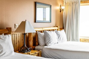A hotel room with a wooden headboard, a bedside table with a lamp, a clock, and a bed with white bedding.