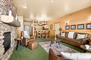 A cozy living room with a stone fireplace, leather sofas, a dining area, and a kitchen in the background.