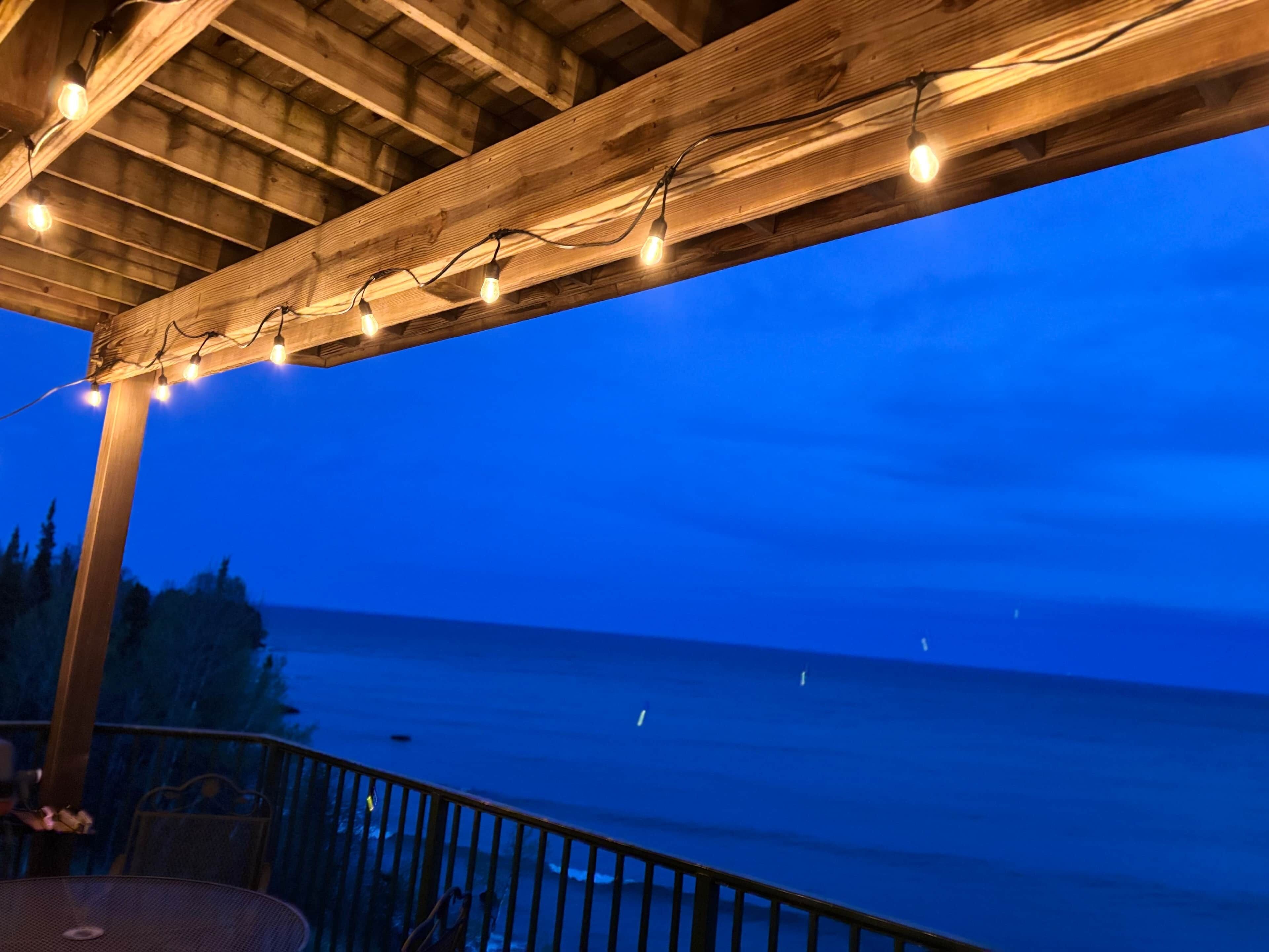 Une terrasse en bois, illuminée de guirlandes lumineuses, qui offre une vue sur une étendue d’eau.