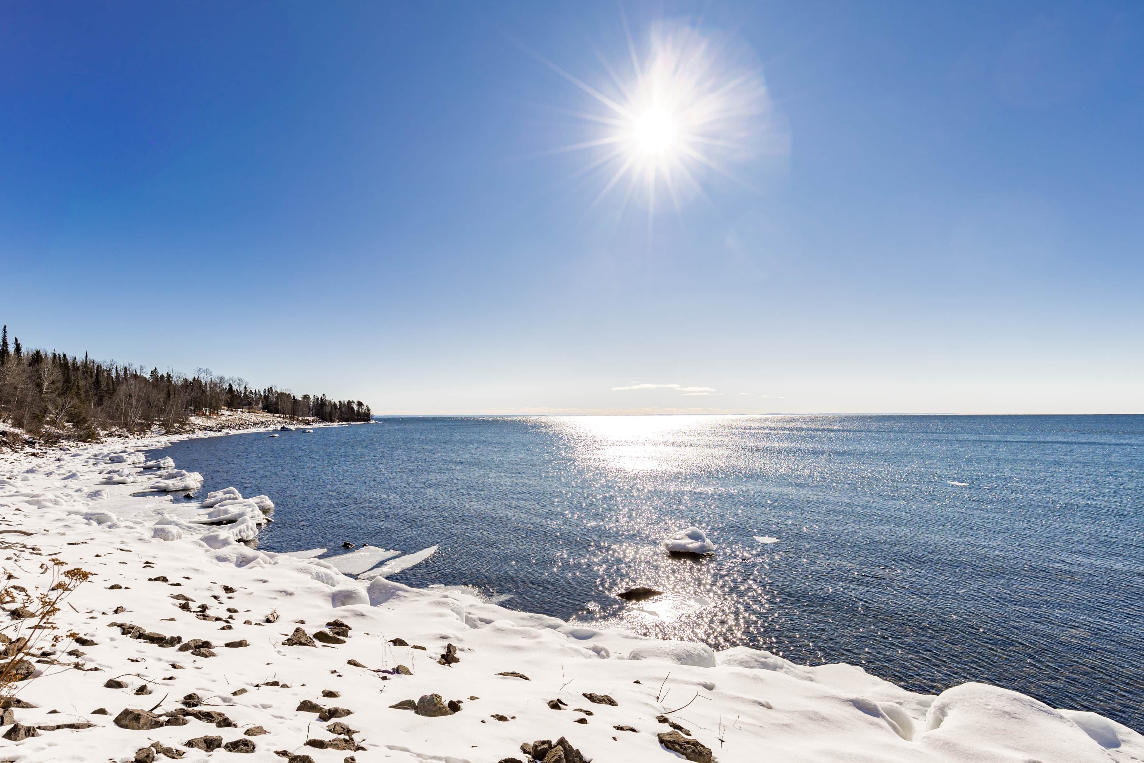 A snowy beach with a clear sky and calm water.