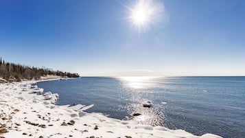 A snowy beach with a clear sky and calm water.