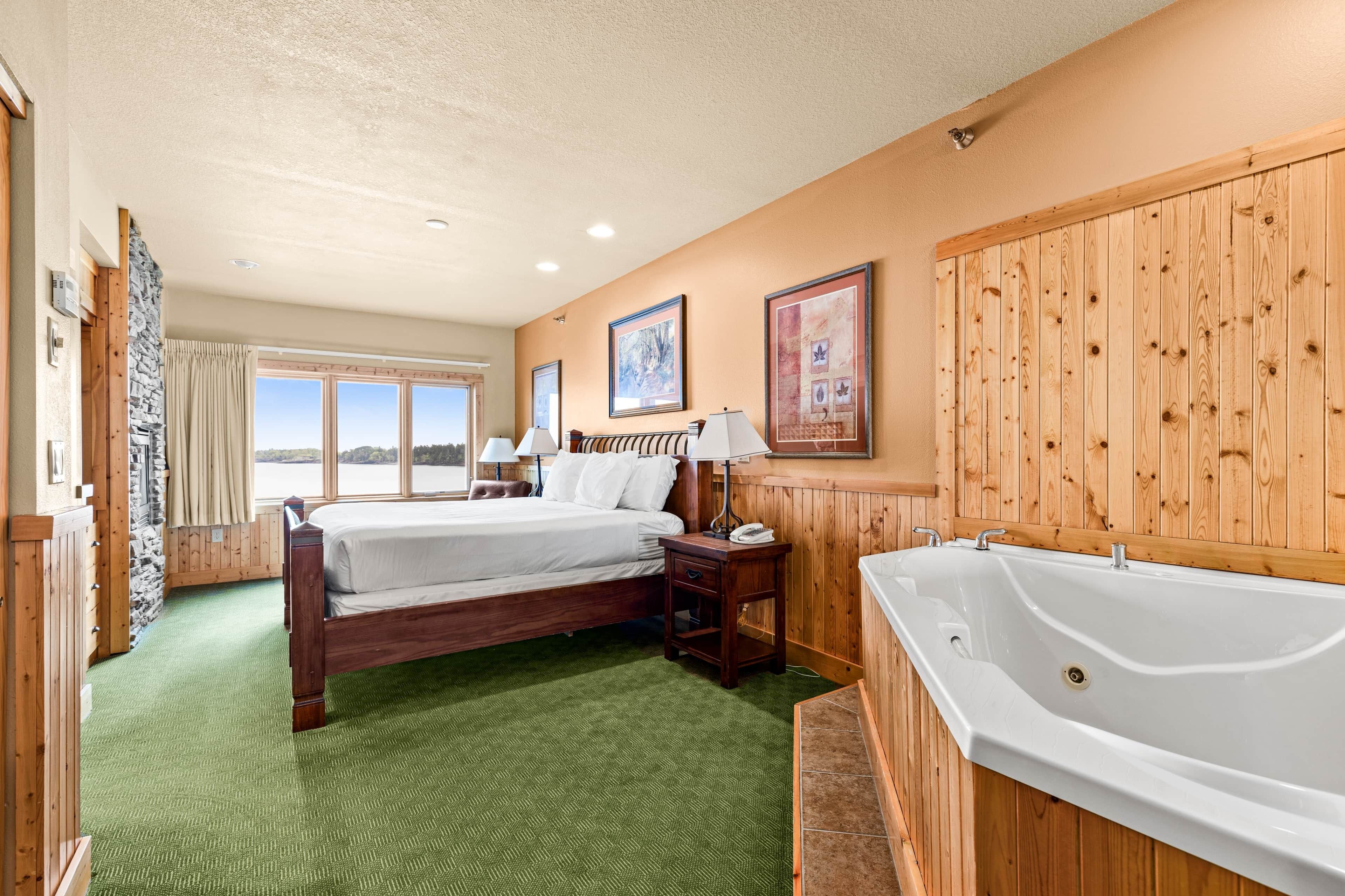 Ein Hotelzimmer mit einem großen Bett, Holzvertäfelung, einer Badewanne und Blick ins Freie durch das Fenster.
