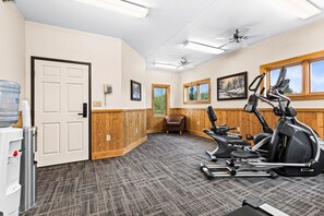 A gym with exercise equipment, a water dispenser, and a wooden-paneled wall. - Amazing Lake Views | 1BR w/ King Suite | Pools (Two Harbors)