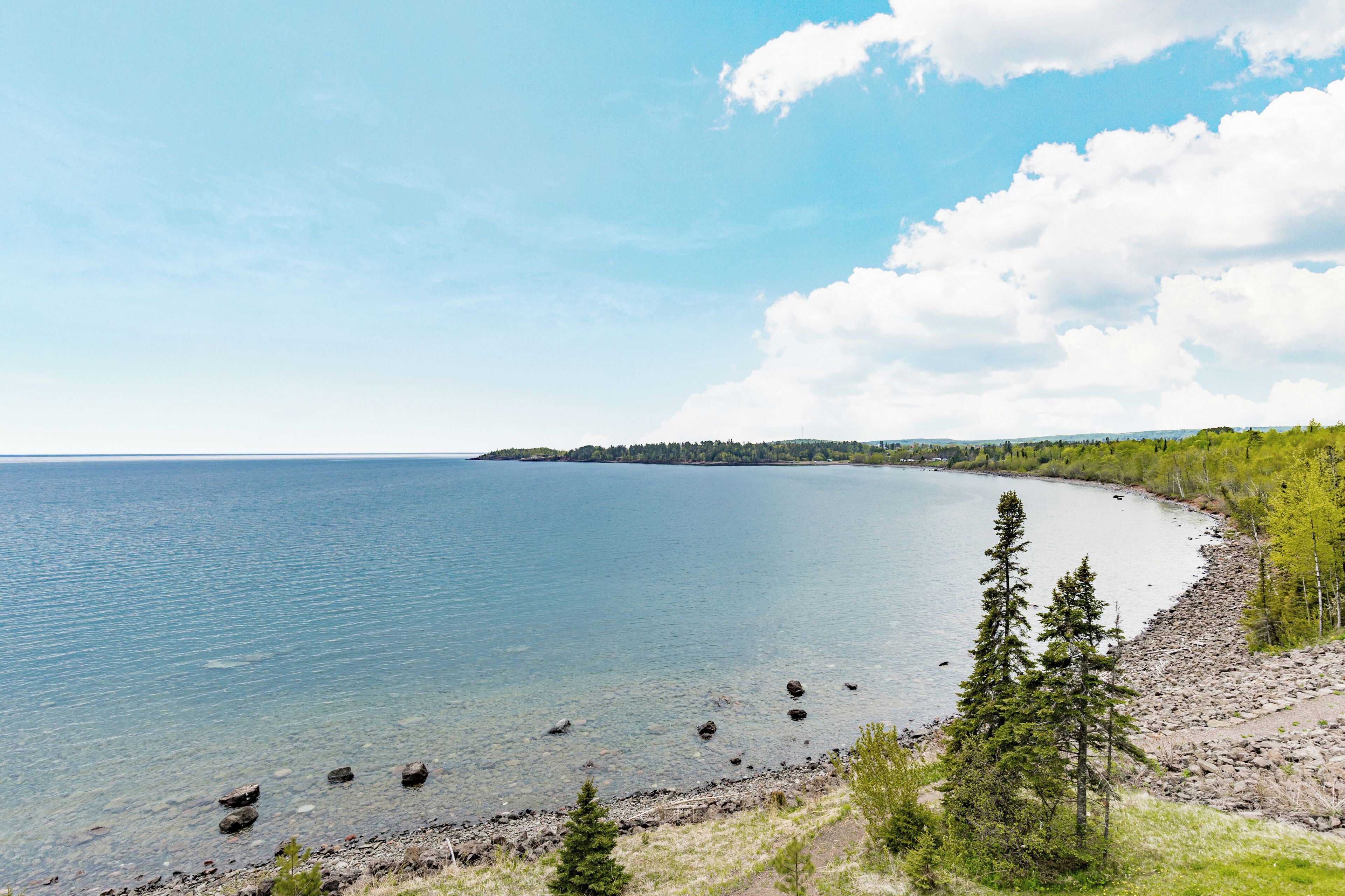 A coastal landscape with a clear view of the water, a rocky shoreline, and a forested area.
