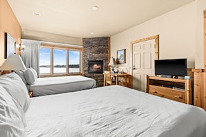 Habitación de hotel con dos camas, chimenea de piedra, televisor y vistas al exterior.