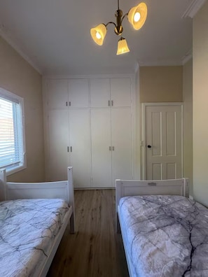 A bedroom with two beds, a wardrobe, a door, and a ceiling light fixture. - Cozy Mountain Cottage (Katoomba)