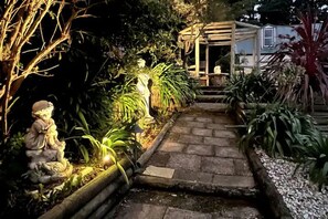 A garden pathway leading to a wooden structure with a statue and plants. - Cozy Mountain Cottage (Katoomba)