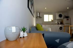 A compact living space with a bed, a small table with a vase and a plant, and a kitchenette in the background. - Cozy Mountain Cottage (Katoomba)